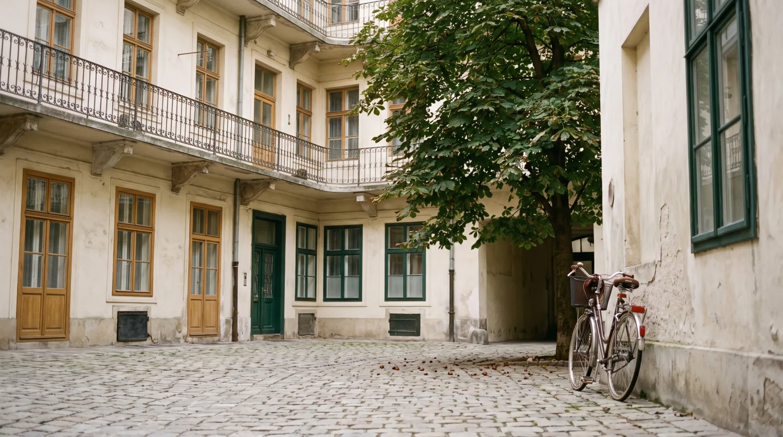 KI-generiertes Bild: Ein ruhiger Innenhof eines Wiener Altbaus im Morgenlicht, mit Kastanienbaum, Fahrrad und Kopfsteinpflaster.